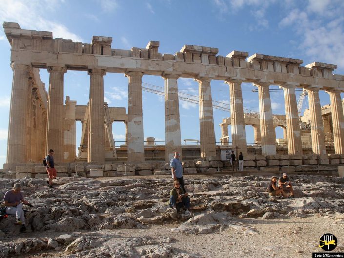Les visiteurs explorent les ruines du Parthénon sous un ciel bleu clair, certains reposant sur un terrain rocheux au premier plan, s'imprégnant de la splendeur antique à Athènes en Grèce.