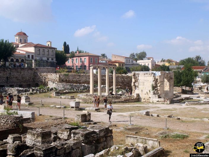 Ruines antiques avec colonnes en ruine et structures en pierre entourées de bâtiments modernes et d'une église avec un dôme en arrière-plan à Athènes en Grèce. Les visiteurs se promènent et explorent le site.