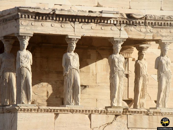 Une section d'un temple grec antique, situé à Athènes en Grèce, avec des colonnes sculptées comme des figures féminines drapées, connues sous le nom de Cariatides, soutenant un entablement en pierre.