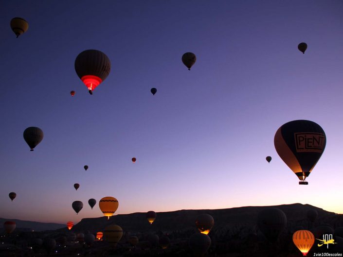 Montgolfières de différentes couleurs et motifs flottant à l'aube près d'un paysage montagneux en Cappadoce en Turquie.