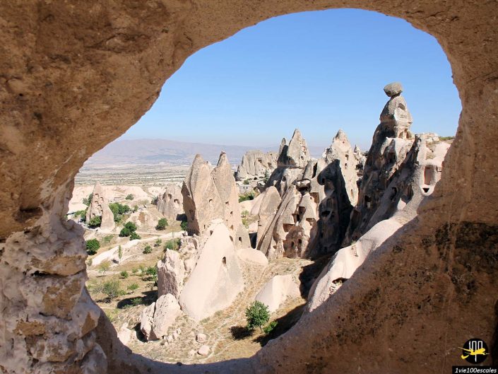 Vue du paysage rocheux en Cappadoce en Turquie, vu à travers une ouverture de grotte, avec des formations rocheuses pointues sous un ciel bleu clair.
