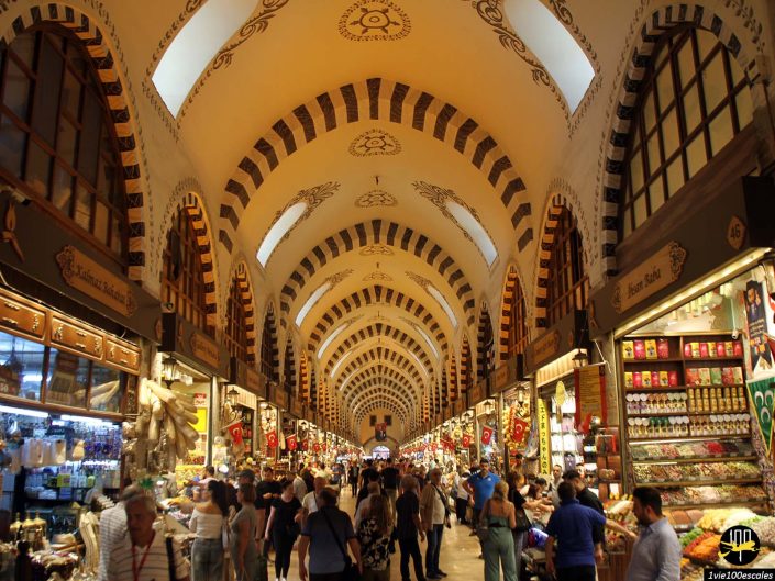 Les gens font leurs courses dans un marché animé avec des plafonds voûtés et divers stands de chaque côté vendant des marchandises, à Istanbul en Turquie.