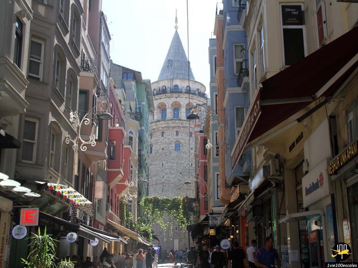 Une rue étroite bordée de bâtiments colorés mène à la tour historique de Galata à Istanbul en Turquie, avec des gens marchant au soleil.
