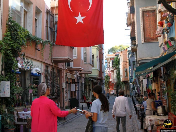 Une rue à Istanbul en Turquie avec des passants, un grand drapeau turc affiché au-dessus et divers magasins bordant les deux côtés.