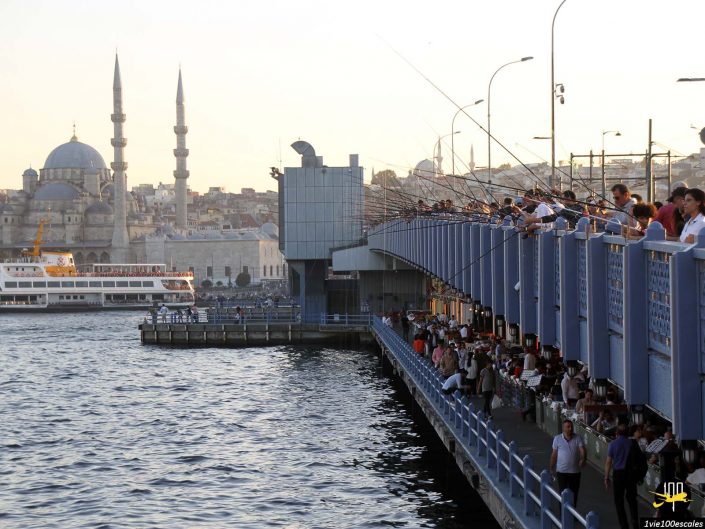 Des gens pêchant sur un pont bondé avec un paysage urbain comportant des mosquées avec des minarets en arrière-plan, à Istanbul en Turquie.
