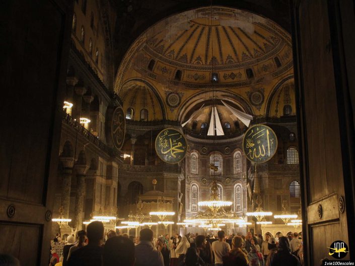Une foule nombreuse à l'intérieur d'un bâtiment historique avec des plafonds en forme de dôme ornés, des lustres et des décorations en écriture arabe sur des plaques circulaires, à Istanbul en Turquie.