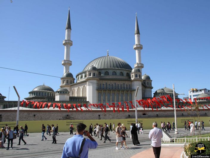 Des gens marchent sur une place près d’une grande mosquée aux multiples minarets à Istanbul en Turquie. Des drapeaux rouges sont déployés dans la zone ouverte.