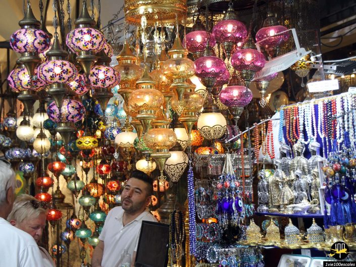 Homme sur un stand de marché à Istanbul en Turquie, vendant diverses lanternes en verre colorées et objets en perles suspendus au plafond et exposés sur des étagères.