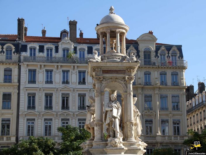 Un monument en pierre détaillé avec des statues se dresse devant un bâtiment historique orné de plusieurs étages avec de nombreuses fenêtres et balcons à Lyon en France.
