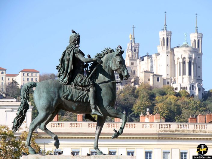 Statue équestre devant des bâtiments historiques et une basilique perchée sous un ciel bleu clair à Lyon en France.