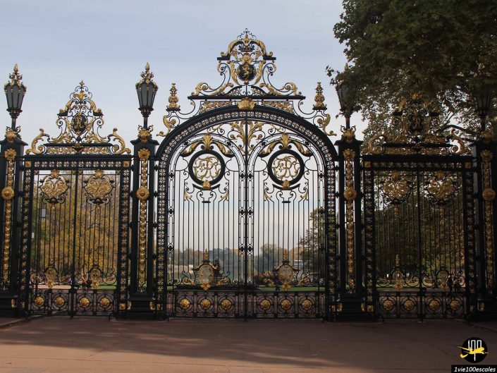 Des portes en fer forgé élaborées ornées d'accents dorés accueillent les visiteurs dans un charmant parc à Lyon en France, avec des arbres et un sentier visible au-delà.