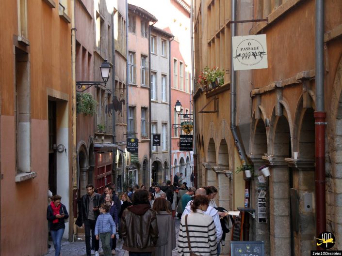Une rue pavée étroite à Lyon en France avec des bâtiments historiques. Les gens marchent, certains regardant les menus et les panneaux indiquant les restaurants et les magasins à proximité.