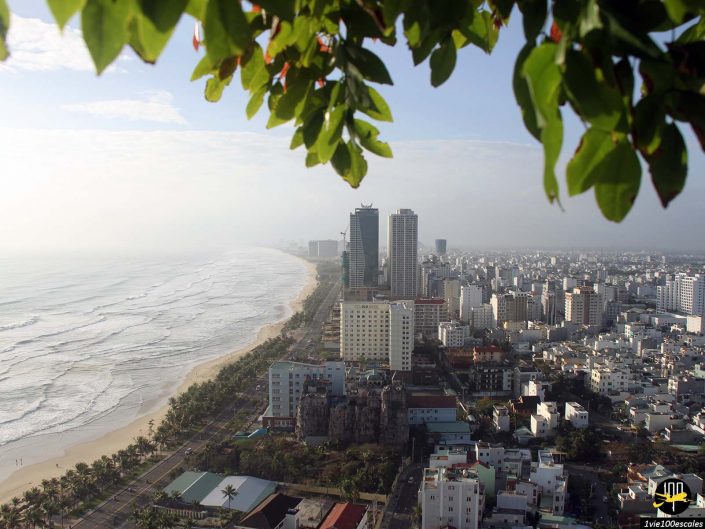 Un paysage urbain côtier présentant de grands immeubles et des zones résidentielles le long du littoral à Da Nang, au Vietnam, avec l'océan à gauche et la verdure encadrant le haut de l'image.