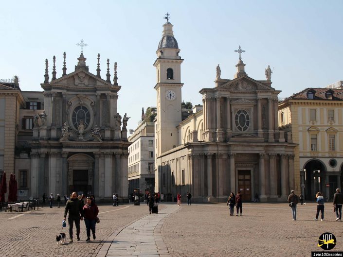 Une grande place pavée avec des passants, bordée par deux églises ornées de tours par temps clair, à Turin en Italie.