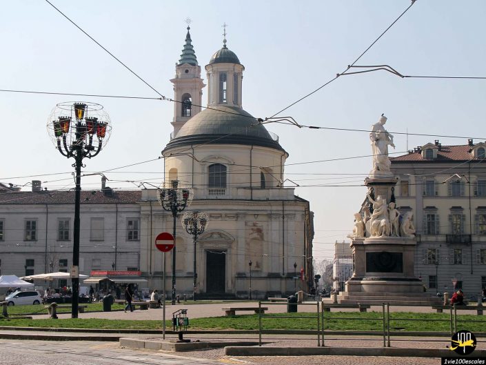 Une église ronde avec un dôme central et un clocher se dresse sur une place avec un grand monument, entourée de bâtiments classiques et de lampadaires à Turin en Italie.