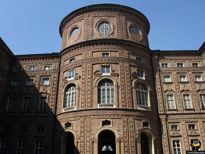 Bâtiment en briques brunes avec une section cylindrique centrale ornée de fenêtres circulaires et de détails architecturaux complexes, situé à Turin en Italie. La façade présente des fenêtres cintrées symétriques et des éléments décoratifs.