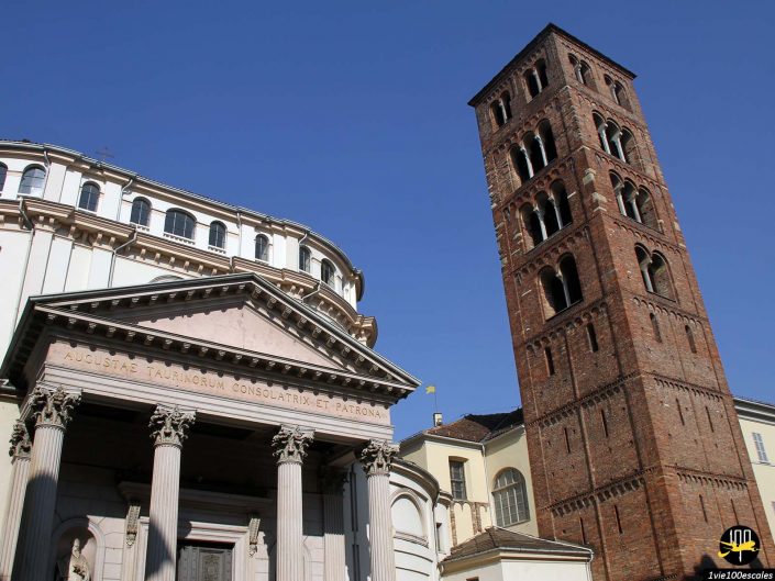 Un bâtiment historique à Turin en Italie présente un portique avec des colonnes à côté d'un haut clocher en brique sous un ciel bleu clair.