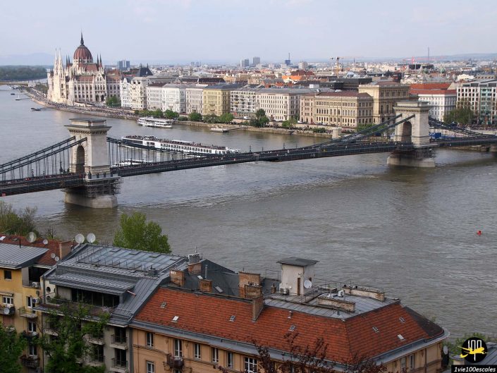 Vue sur le pont des chaînes traversant le Danube avec le bâtiment du Parlement hongrois et le paysage urbain de Budapest en arrière-plan. Les toits des bâtiments sont visibles au premier plan, capturant une scène pittoresque à Budapest en Hongrie.