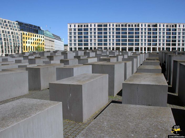 Image du Mémorial aux Juifs assassinés d'Europe à Berlin en Allemagne, composé de nombreux blocs de béton rectangulaires disposés en grille avec des bâtiments modernes en arrière-plan.