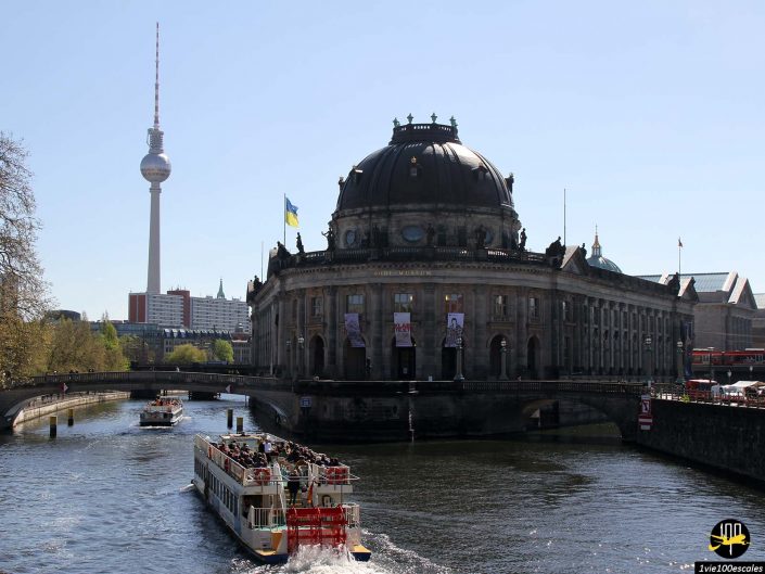 Un bateau fluvial passe devant le musée Bode sur la rivière Spree à Berlin en Allemagne, avec la tour de télévision visible en arrière-plan.