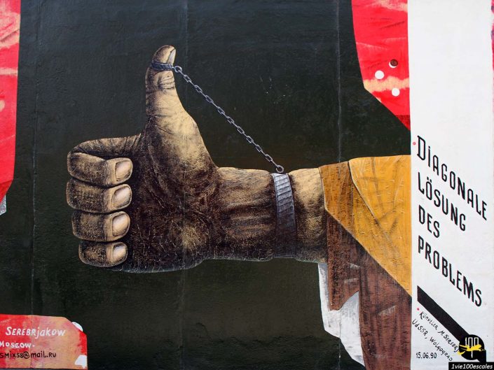 Illustration d'une main tendue avec un geste du pouce levé, partiellement entourée d'une manille. Le texte en allemand à droite indique "DIAGONALE LÖSUNG DES PROBLEMS" à Berlin en Allemagne.