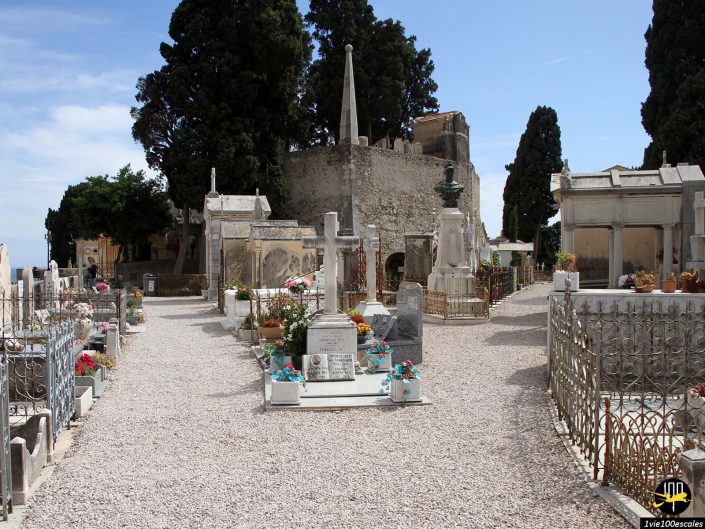 Un cimetière historique à Menton, en France, avec des pierres tombales, des monuments et des mausolées entourés d'allées de gravier et d'arbres.