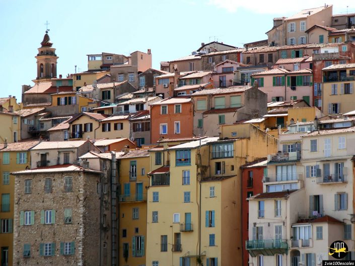 Une colline densément peuplée de bâtiments colorés aux styles architecturaux variés, encadrés par un ciel bleu clair à Menton en France.