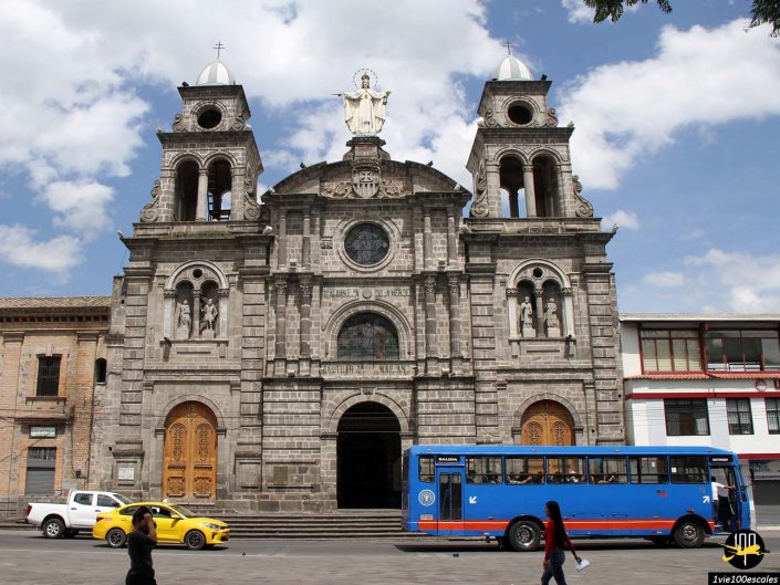 Une église historique en pierre avec des statues et des portes cintrées se dresse magnifiquement à Ibarra en Équateur. Devant, un bus bleu, un taxi jaune et quelques piétons sont visibles.