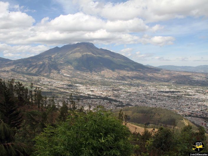 Une grande montagne pittoresque se dresse sous un ciel partiellement nuageux, surplombant la ville tentaculaire d'Ibarra en Équateur et son paysage environnant avec une végétation verte variée.