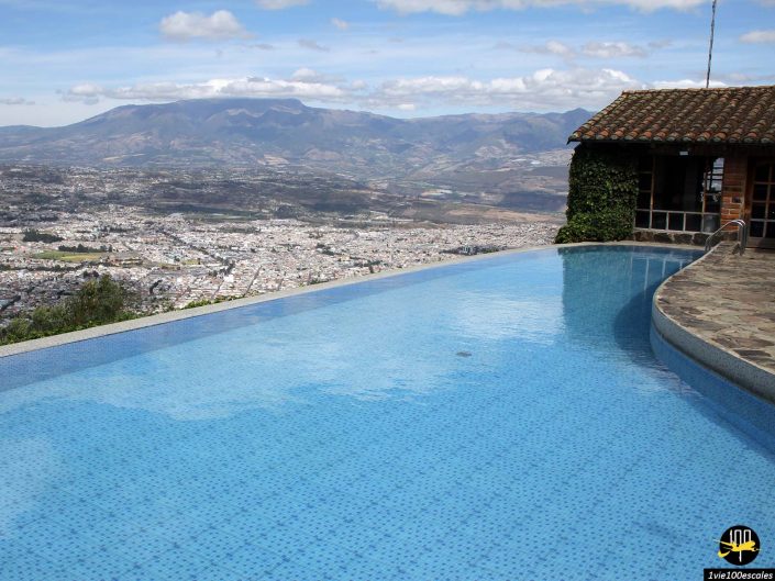 Une piscine à débordement surplombe un vaste paysage, avec des montagnes et une ville visibles en arrière-plan sous un ciel partiellement nuageux à Ibarra en Équateur.