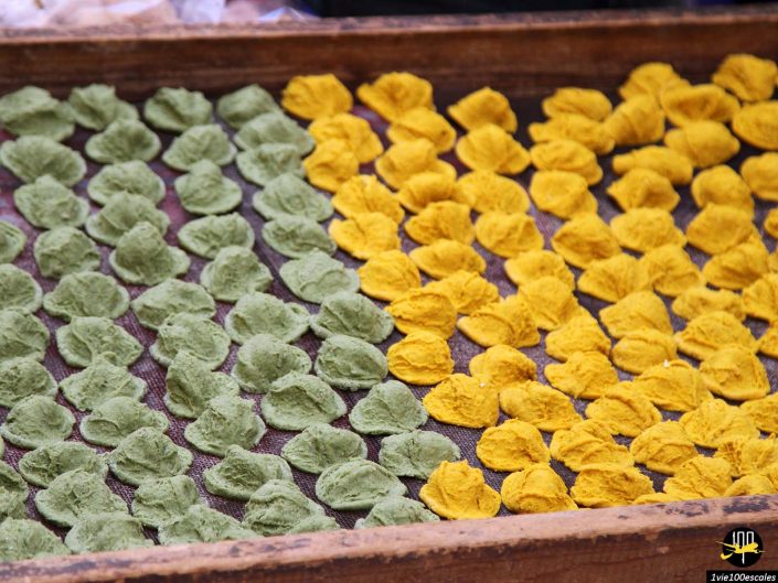 Des rangées de produits alimentaires séchés verts et jaunes sont soigneusement disposées sur un grand plateau en maille, rappelant les marchés de Bari en Italie.