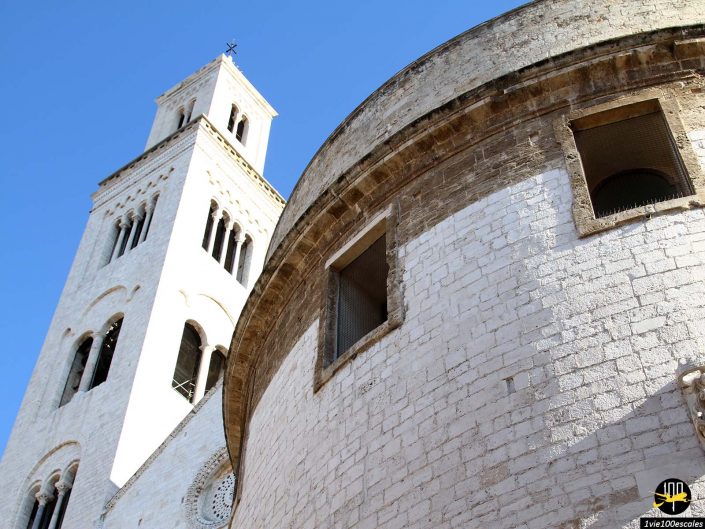 Gros plan d'une église en pierre blanche avec une section cylindrique et un haut clocher sur un ciel bleu clair, située à Bari en Italie.