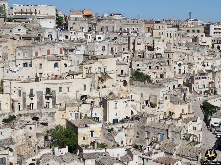 Une ville à flanc de colline densément peuplée avec de nombreux bâtiments en pierre et des rues étroites, de couleur beige uniforme, à Matera en Italie. Certaines maisons disposent d'un balcon et la verdure est rare.