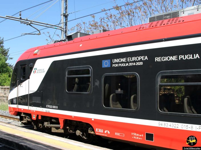 Un train moderne rouge et noir avec les textes « Unione Europea Por Puglia 2014-2020 » et « Regione Puglia » sur le côté, garé sur un quai de gare à Locorotondo en Italie.