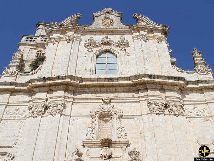 Une façade de bâtiment ornée de couleurs claires de style baroque avec des sculptures et des balcons complexes, sur un ciel bleu clair à Ostuni en Italie.