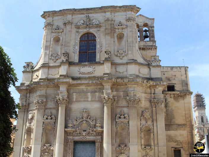 Une façade en pierre détaillée d'un bâtiment historique à Lecce en Italie, avec des éléments architecturaux élaborés, des colonnes ornées et des sculptures décoratives sous un ciel bleu clair.