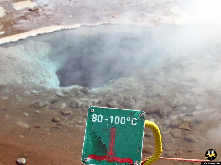 Une source chaude fumante à Islande avec un panneau d'avertissement indiquant des températures de l'eau comprises entre 80 et 100 °C.
