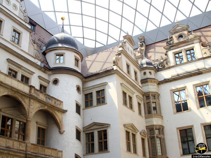 Un bâtiment de plusieurs étages à l'architecture ornée, à Dresde en Allemagne, comporte des fenêtres cintrées, des tourelles et une verrière couvrant la cour intérieure.