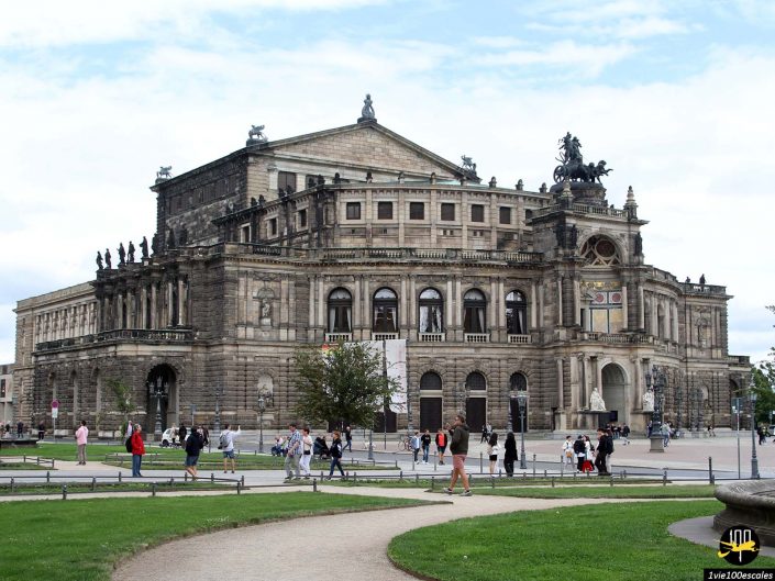 L'image montre le Semperoper à Dresde en Allemagne, un opéra orné avec une conception architecturale historique. Les gens marchent et se rassemblent devant le bâtiment par temps clair.